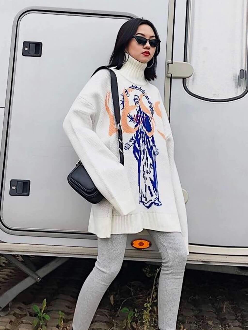 white knitted sweater with the Virgin Mary in blue and her head is surrounded by a large crown of barbed wire. A red inscription is sewn on his chest and the salmon word "LESS" occupies all the space available on the chest worn