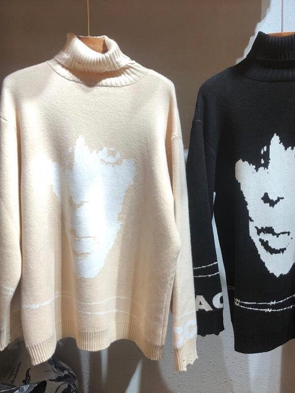 beige knitted sweater with a white face on the front and a barbed wire next to our black knitted sweater with a white face on the front and a barbed wire 