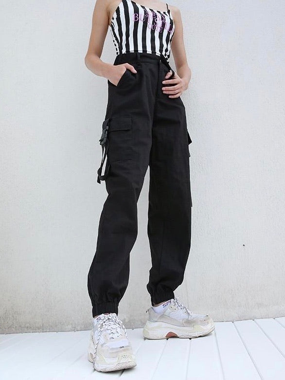 black high waist cargo pants with two big side pockets closed by a plastic buckle strap worn by a woman