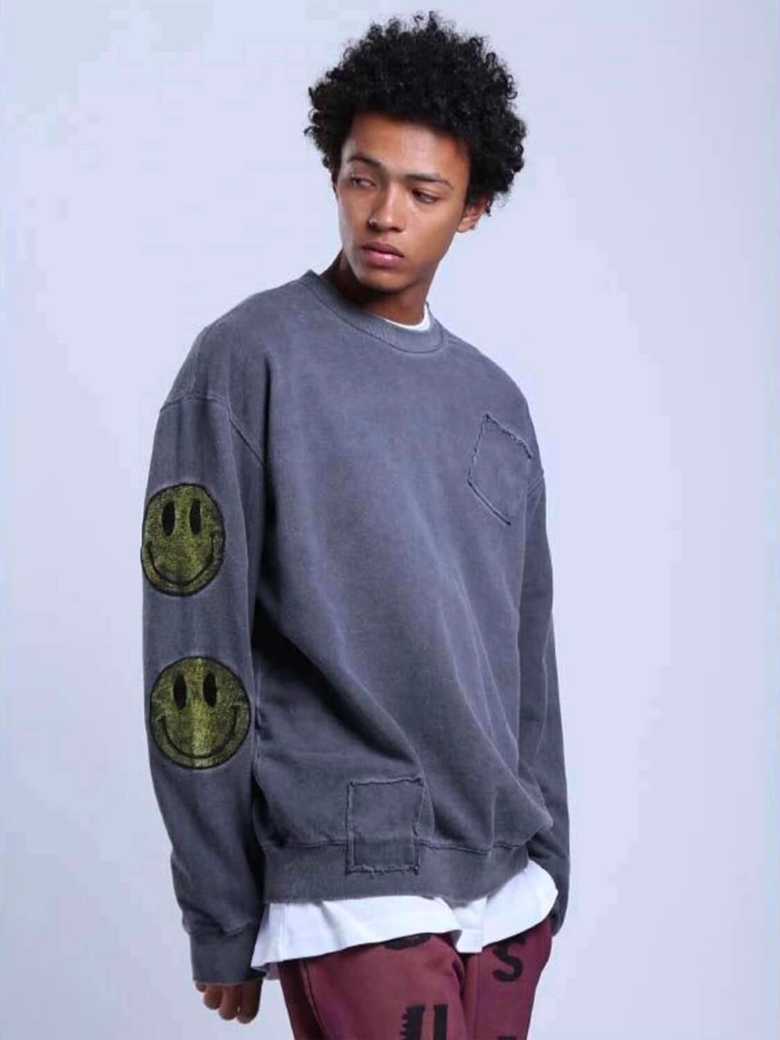 patched gray pullover with large yellow smiling faces on the sleeves and one in the upper back worn