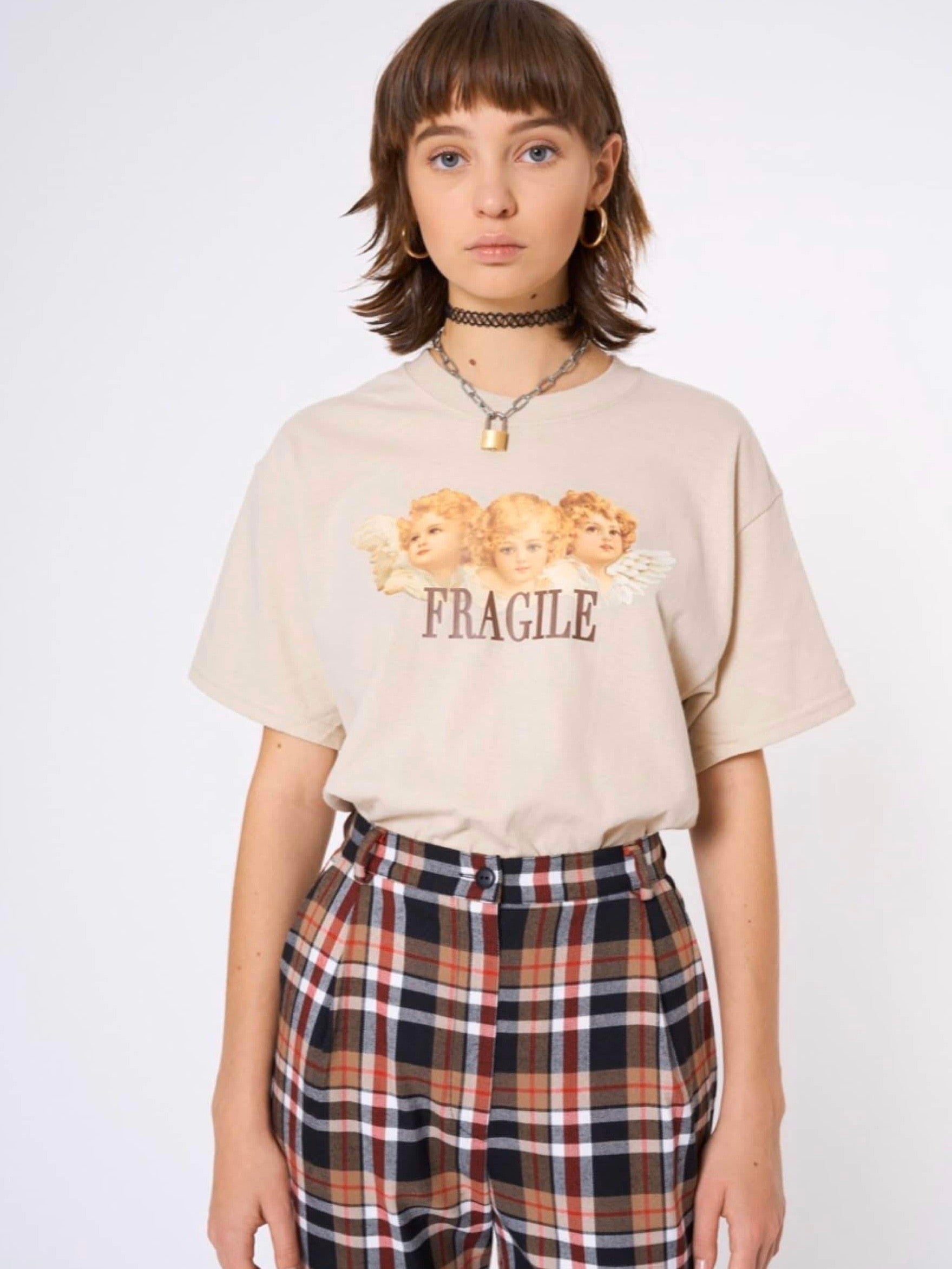 front side of our beige tshirt with three angels printed on the front with the text below fragile in brown