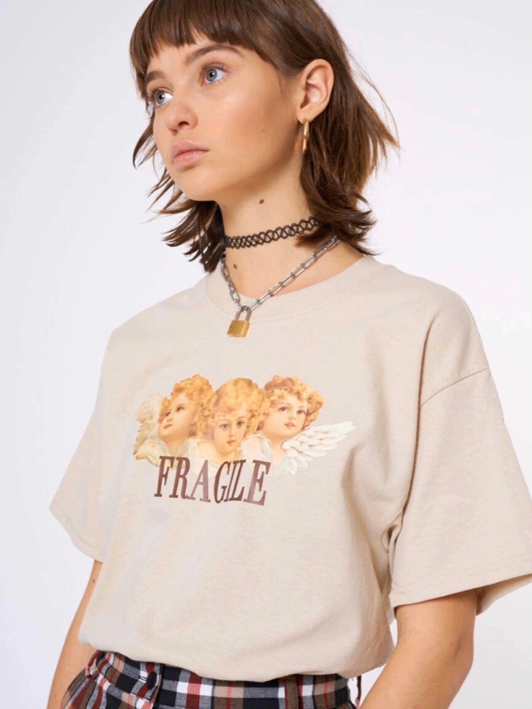 beige tshirt with three angels printed on the front with the text below fragile in brown worn